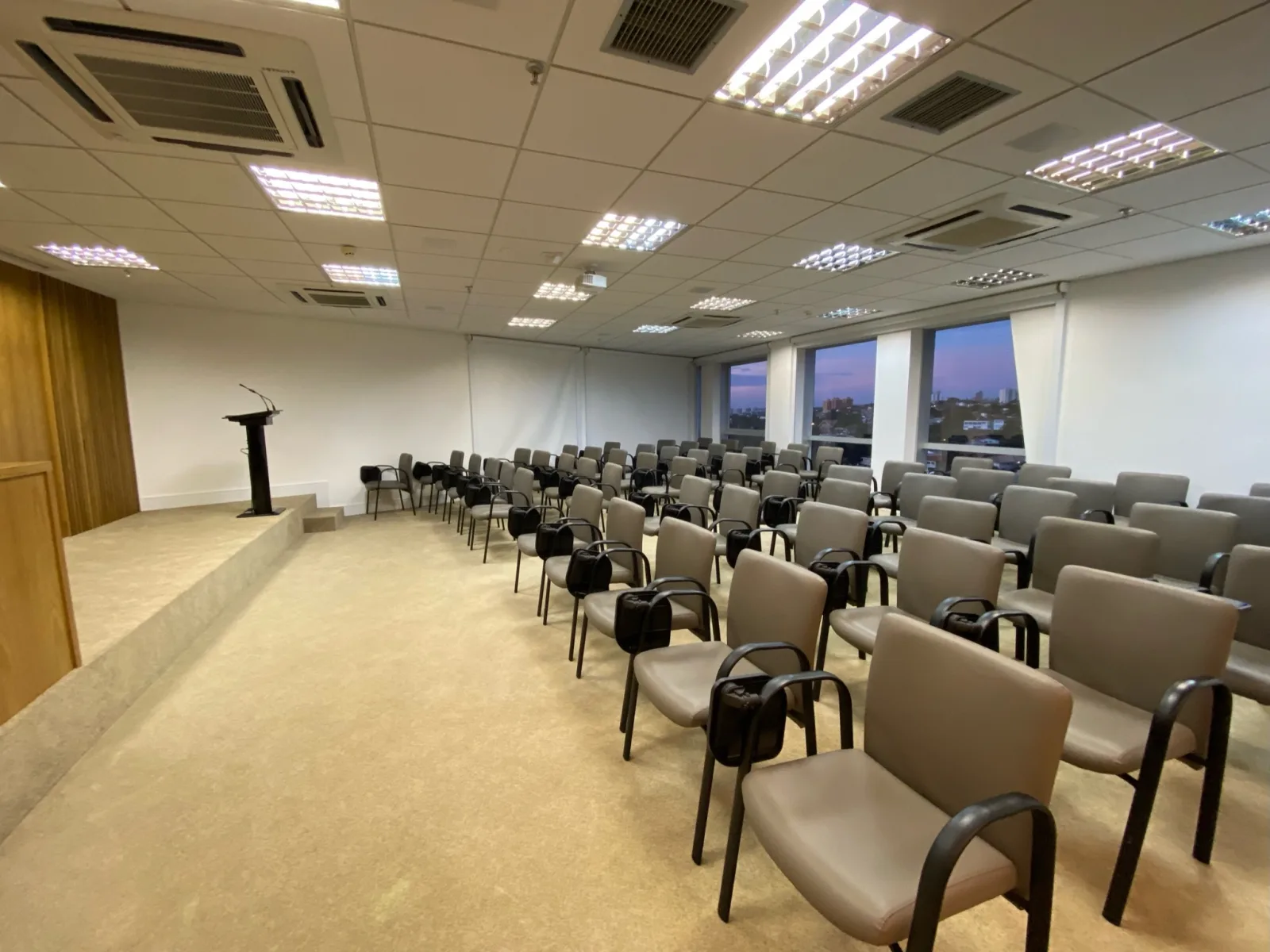 Auditório da Eureka na Norte-Sul 507, em Campinas, com cadeiras em formato palestra, púlpito no palco e vista da cidade pelas janelas